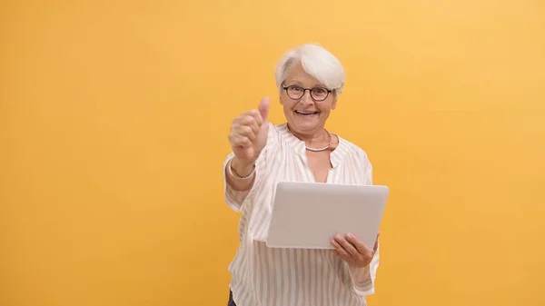 Sonriendo feliz mujer mayor mostrando los pulgares hacia arriba después de mirar la pantalla del ordenador portátil — Foto de Stock