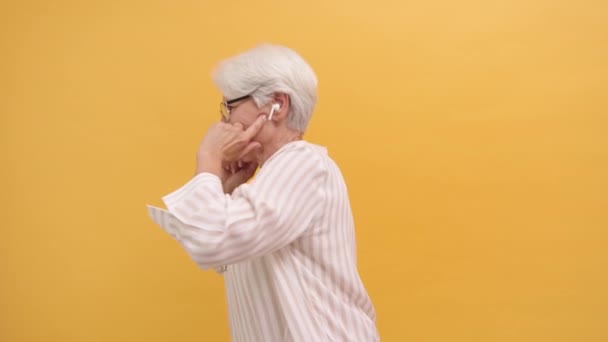 Drôle de vieille femme heureuse dansant avec des écouteurs sans fil, isolé sur fond orange — Video