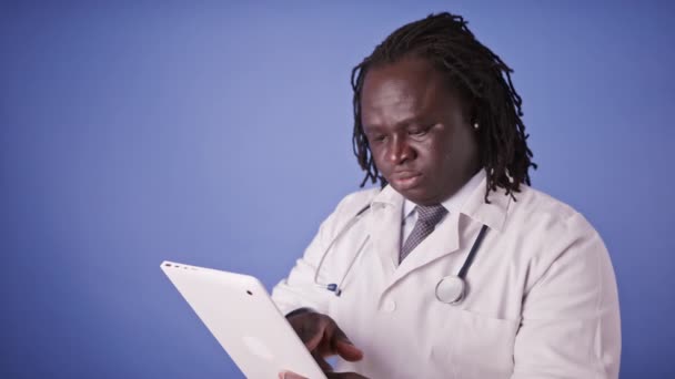 Retrato do médico negro africano que trabalha no comprimido. Movimento lento isolado em azul — Vídeo de Stock