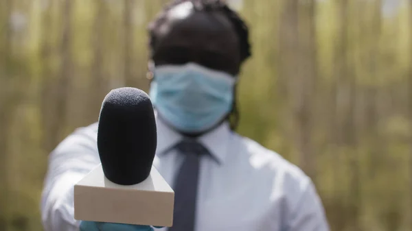 Yüzü tıbbi maskeli ve eldivenli Afrikalı muhabir, koronavirüsün yayıldığını bildiriyor. — Stok fotoğraf
