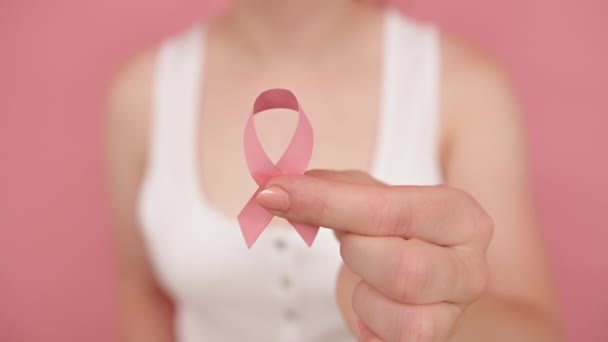 닫고, 실크 핑크 리본을 손가락 사이에 쥐고 있는 여성. 유방암을 인식하는 달 분홍색 동 백체 — 비디오