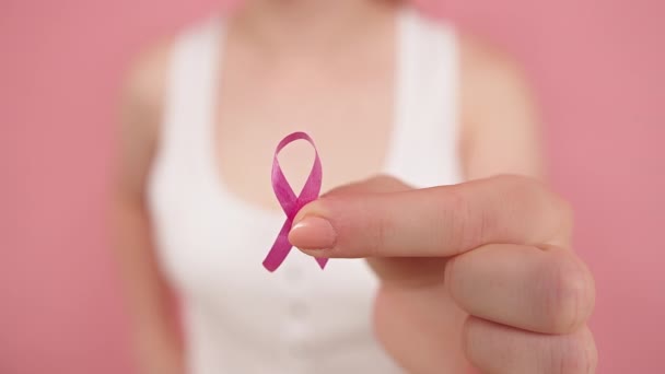 Junge Frau mit symbolischem rosa Band zwischen ihren Fingern. Brustkrebs-Aufklärungsmonat, rosa Oktober — Stockvideo