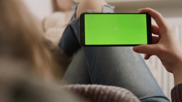 Jeune femme touchant écran vert smartphone tout en se reposant sur le canapé — Video