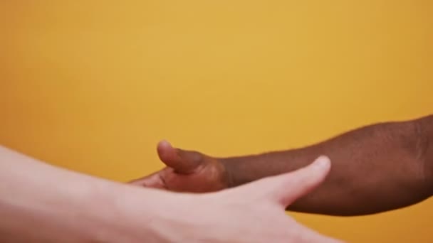 Fekete-fehér kéz tartja össze elszigetelve a narancssárga háttér. Közelről. — Stock videók