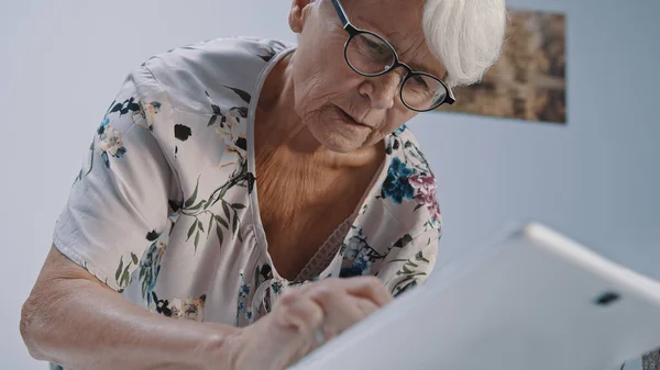 Vieja mujer de pelo gris con anteojos usando la tableta. Disparo de ángulo bajo — Foto de Stock