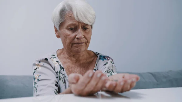 Zaniepokojony dojrzałe siwe włosy kobieta trzyma pigułki w jej rękach — Zdjęcie stockowe