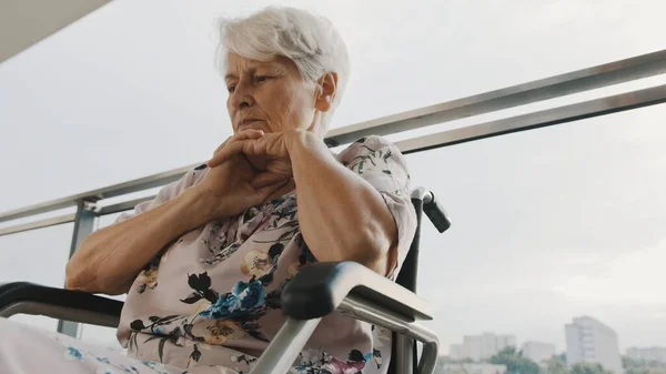 Сидящая в инвалидной коляске больная старушка издалека чувствует себя одинокой дома или в доме престарелых — стоковое фото