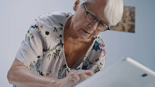 Mujer mayor de pelo gris con anteojos usando la tableta. Disparo de ángulo bajo — Foto de Stock