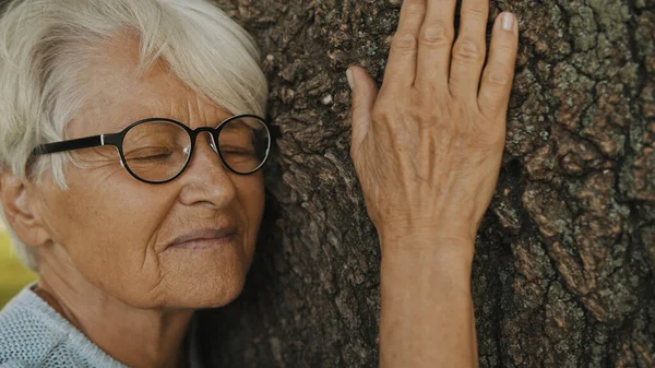 Portret starszej siwowłosej kobiety przytulającej drzewo — Zdjęcie stockowe