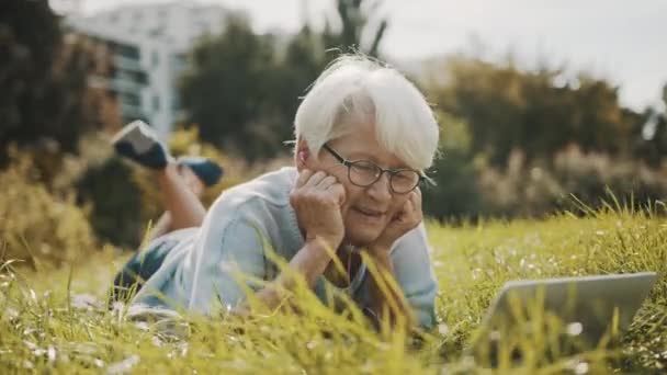 Senior vrouw met een video gesprek terwijl liggend op de herfst gras in het park — Stockvideo