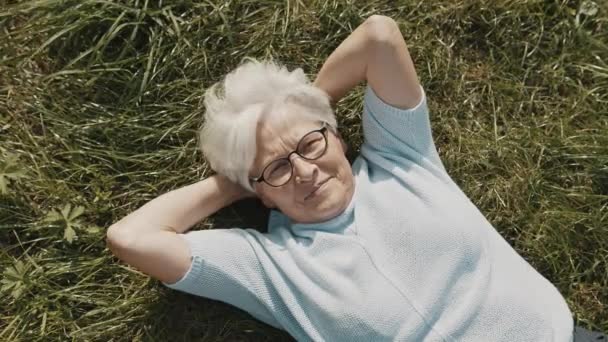 Ηλικιωμένη γυναίκα, συνταξιούχος ξαπλωμένη στο γρασίδι με τα χέρια κάτω από το κεφάλι της στον κήπο από πάνω κοντινό πλάνο. — Αρχείο Βίντεο