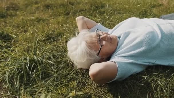 Gammal kvinna som ligger på gräset med händerna under huvudet. närbild skott — Stockvideo