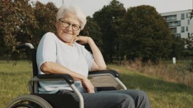 Kıdemli engelli kadın parkta tekerlekli sandalyede oturmuş sonbahar melteminin tadını çıkarıyor.