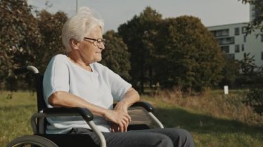 Düşünceli yaşlı engelli kadın parkta tekerlekli sandalyede oturmuş sonbahar melteminin tadını çıkarıyor.