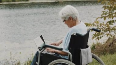 Engelli olgun kadın sonbahar rüzgarlı bir günde nehrin yanındaki bilgisayarı kullanıyor.