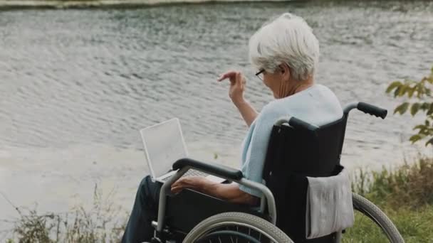 Handicap volwassen vrouw zwaaien naar laptop camera tijdens de video gesprek in de buurt van de rivier — Stockvideo