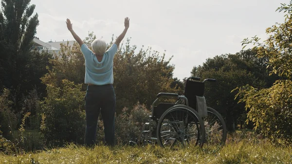 Mujer mayor con las manos extendidas en la naturaleza delante de la silla de ruedas — Foto de Stock