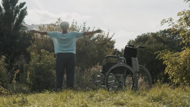 Γριά γυναίκα εξάσκηση στο πάρκο μπροστά από την αναπηρική καρέκλα στη φύση — Αρχείο Βίντεο