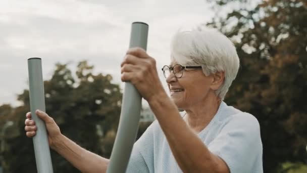 Primer plano de la abuela de pelo gris haciendo ejercicio en el gimnasio al aire libre equipo de parque infantil — Vídeo de stock