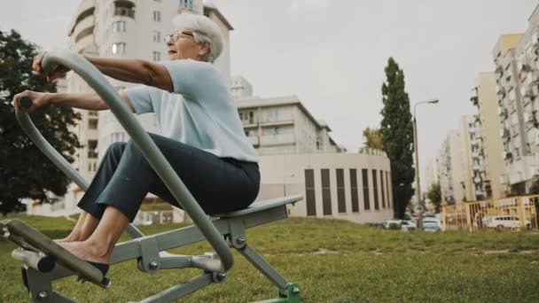 Koncepcja dobrego samopoczucia. Starsza kobieta ćwiczy przy użyciu sprzętu siłowni na świeżym powietrzu — Wideo stockowe