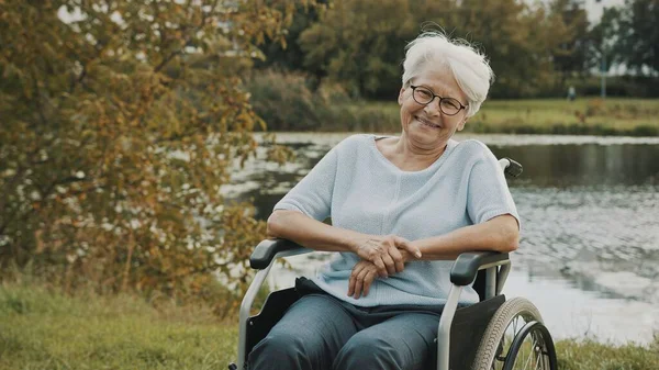 Szczęśliwa babcia na wózku inwalidzkim korzystających jesienny dzień w pobliżu rzeki — Zdjęcie stockowe