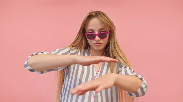 Junge kaukasische Frau mit rosa Sonnenbrille, die Musik hört und tanzt. Isoliert auf dem rosa Hintergrund — Stockfoto