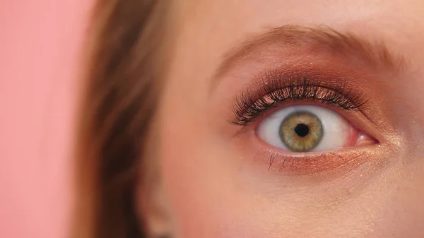 Макро выстрел испуганный удивленный зеленый глаз женщины с тенью для глаз изолированы на розовом фоне — стоковое фото