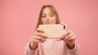 Beyaz bir kadın akıllı telefon kullanıyor ve fotoğraf çekiyor. Pembe arka planda izole edilmiş