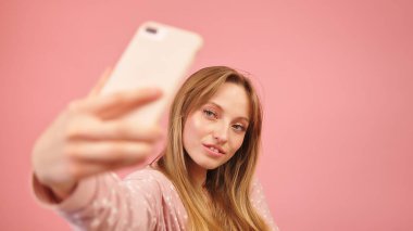 Pijamalı genç kız akıllı telefonu kullanarak selfie çekiyor. Pembe arka planda izole edilmiş