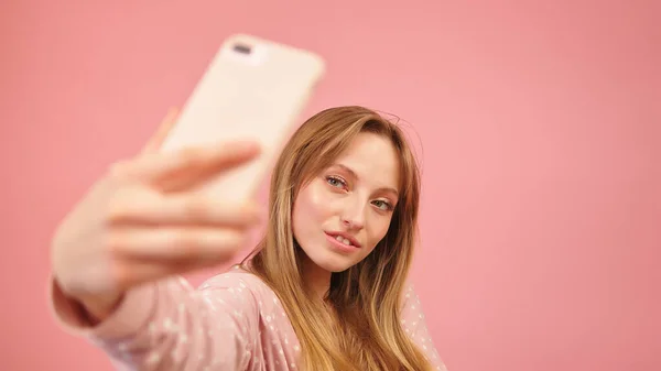 Adolescente de pijama tirando selfies usando o smartphone. Isolado sobre fundo rosa — Fotografia de Stock