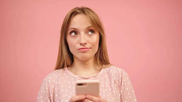 Jovem caucasiana de pijama usando smartphone, isolado em fundo rosa — Fotografia de Stock