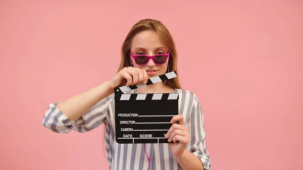 Ung kaukasisk kvinna med rosa solglasögon håller en klassisk svart film clapperboard — Stockfoto