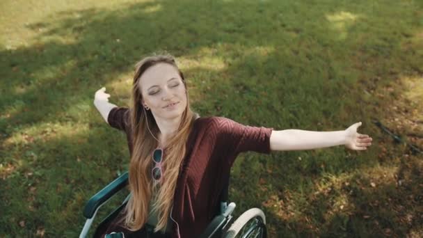 Junge behinderte Kaukasierin im Rollstuhl genießt die frische Luft im Park mit Musik vom Smartphone — Stockvideo