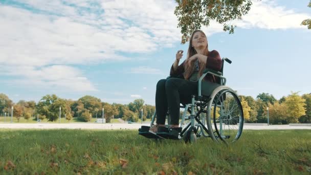 Νεαρή καυκάσια ανάπηρη γυναίκα ακούει μουσική και χορεύει στο χέρι κάτω από το δέντρο. ευρεία γωνία — Αρχείο Βίντεο