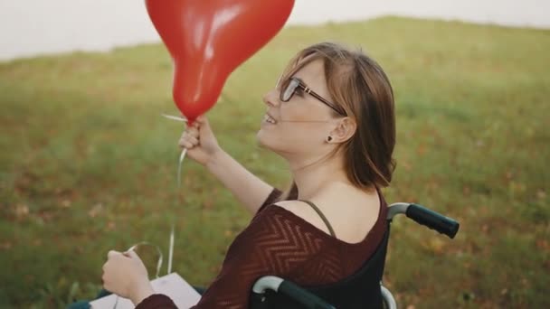 Gehandicapte blanke jonge vrouw met rode ballon kijken over de schouder en glimlachen — Stockvideo