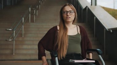 Tekerlekli sandalyedeki merdivenlerin önünde üzgün, yardıma muhtaç genç bir kadın var. Erişilemeyen alan