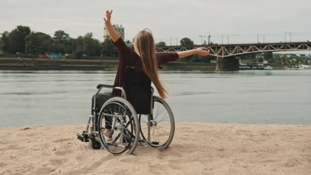 Feliz joven discapacitada en silla de ruedas disfrutando de las vacaciones en la costa del río arenoso — Vídeo de stock