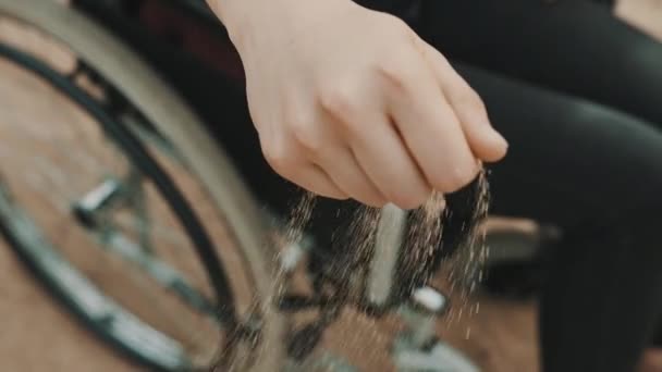 Närbild, handikappade personers hand i rullstolen leker med sanden på stranden — Stockvideo