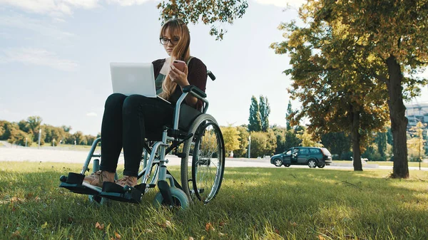 Remote work concept. Young disabled woman in the wheelchair using smartphone and laptop