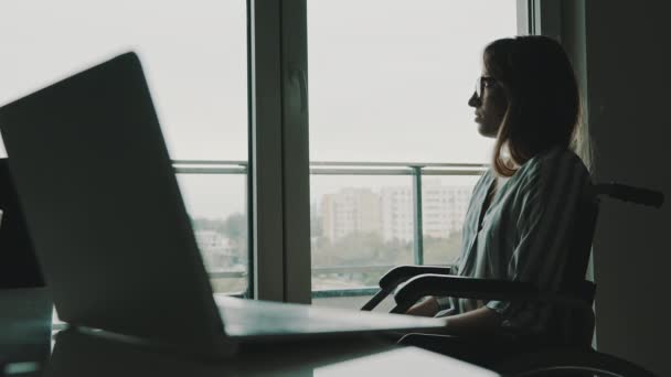 Mujer discapacitada joven deprimida cerca de la ventana mirando lejos de la computadora portátil. — Vídeos de Stock