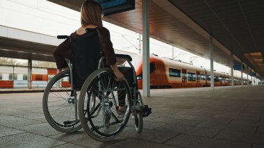Engelli genç kadın tekerlekli sandalyede tren bekliyor.