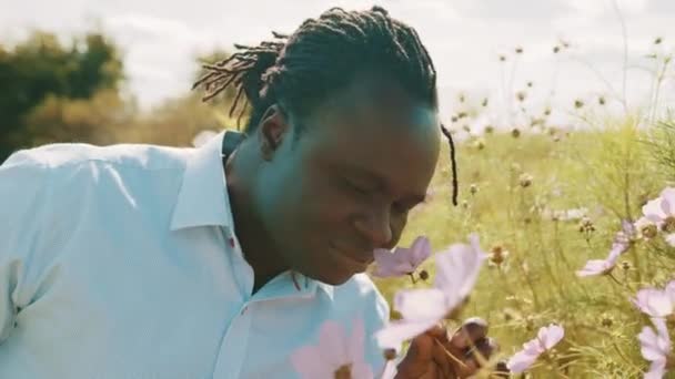 Hermoso joven agricultor africano oliendo flores moradas en la granja — Vídeos de Stock