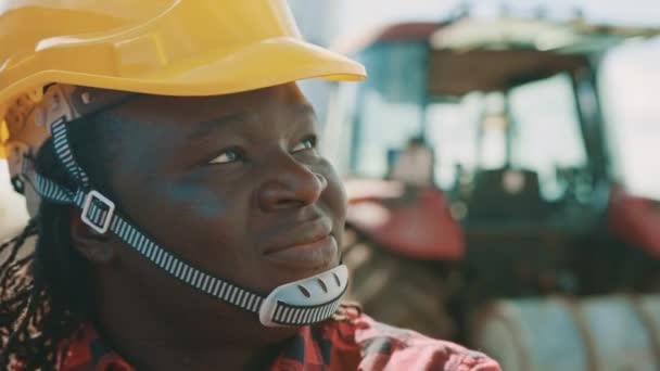 Afrikansk man med skyddshjälm som ser ut som en arond på gården. Traktor i baksätet — Stockvideo