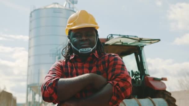 Retrato del feliz agricultor africano frente al sistema de silos y tractores — Vídeos de Stock