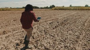 Genç Afrikalı çiftçi elinde tabletle çiftlikte yürüyor.