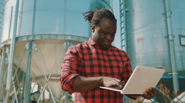 Silo depolama sisteminin önünde dizüstü bilgisayar kullanan Afrikalı çiftçi