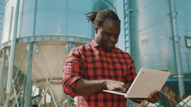 Αφρικανός αγρότης που χρησιμοποιεί φορητό υπολογιστή μπροστά από το σύστημα αποθήκευσης σιλό — Αρχείο Βίντεο