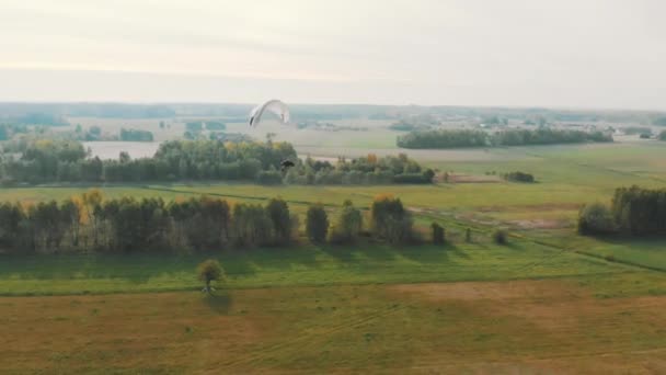 Flygfoto av en paramotor glider genom luften över gröna fält — Stockvideo