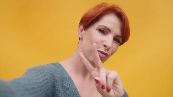 Mulher de cabelo vermelho ter uma chamada de vídeo, mostrando sinal de paz com sorriso — Fotografia de Stock