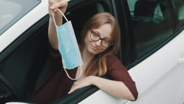 Een jonge blanke vrouw die een medisch masker uit haar auto gooit. Einde van de covid-19 pandemie — Stockvideo